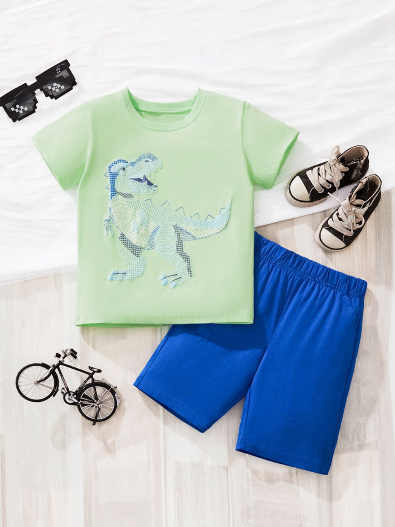 Children's light green cotton tee with dinosaur graphic and blue shorts.