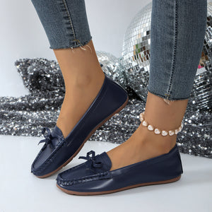 Dark blue slip-on loafers with bow detail and contrast stitching.