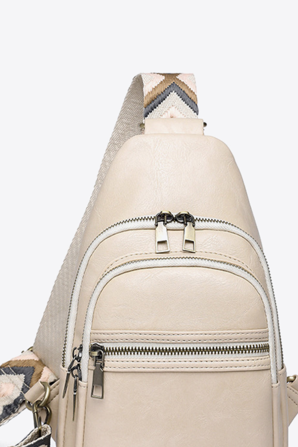 Cream geometric strap sling bag with multiple zippered compartments and metal hardware.