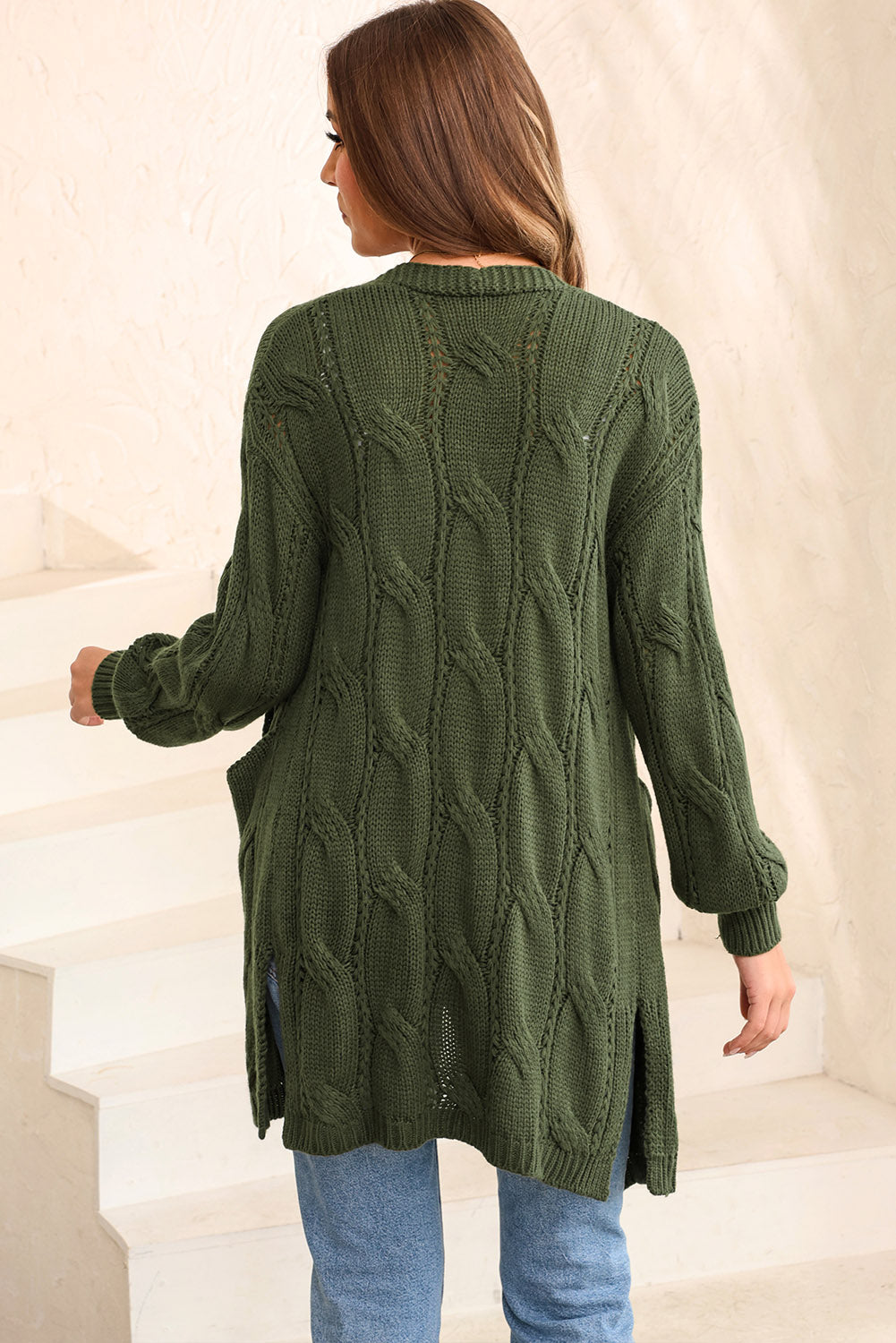 Green cable knit open-front cardigan with pockets and side slits.