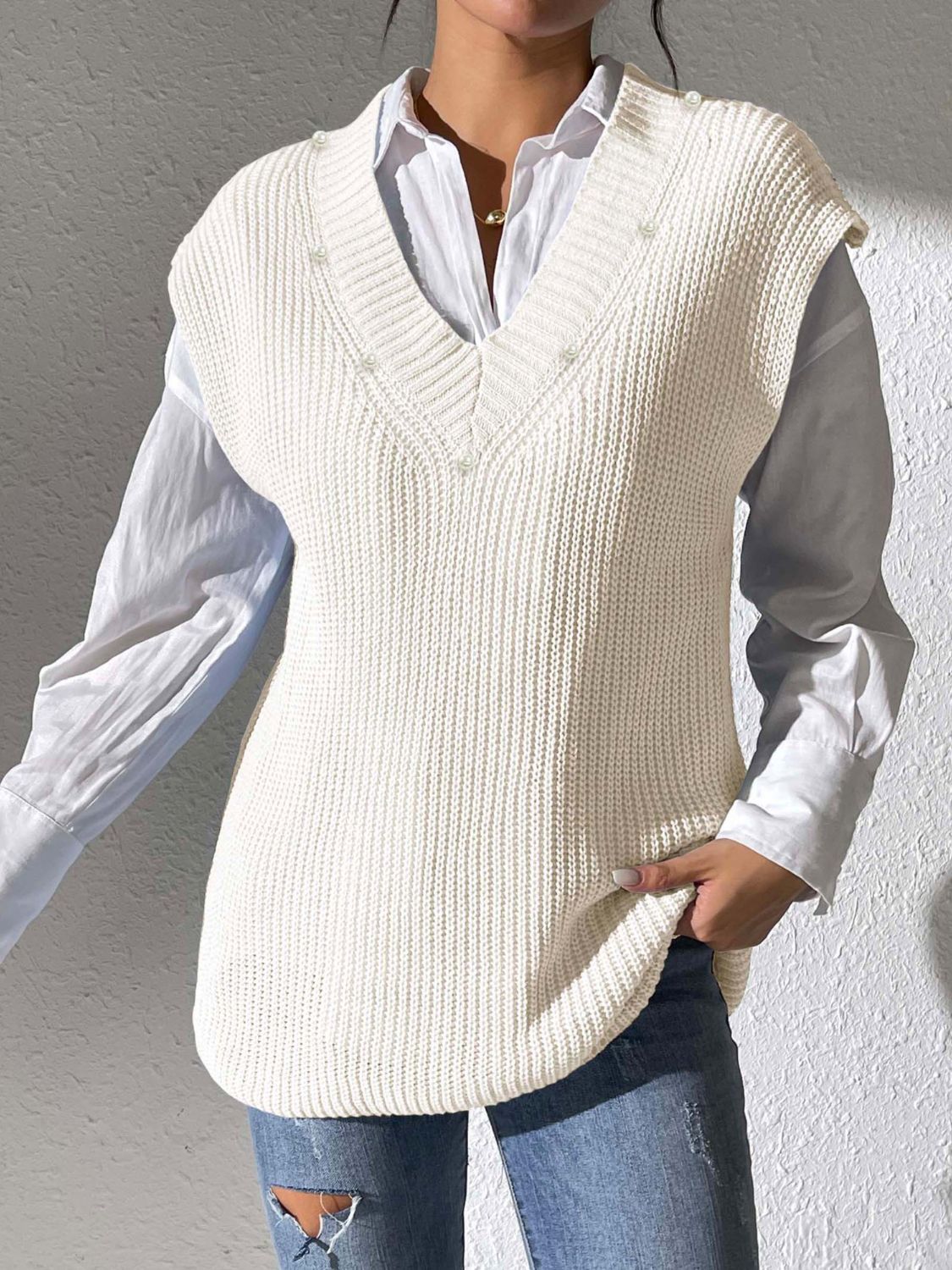 Ivory ribbed knit sleeveless V-neck vest with pearl embellishments, styled over a white shirt.