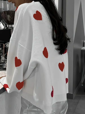 White oversized knit crewneck sweater with red heart pattern and drop sleeves.