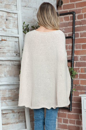 Cream knit cape sweater with wide sleeves and scalloped hem, styled with jeans.