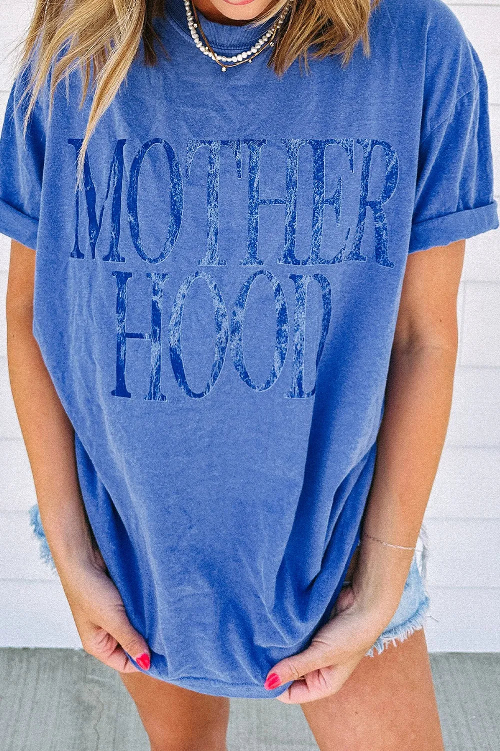 Blue oversized graphic t-shirt with "Motherhood" text, cuffed sleeves, and crew neck.