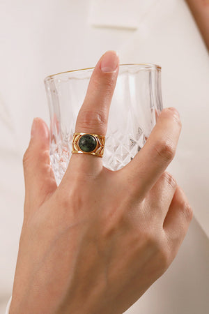 Gold ring with malachite stone and leaf-cut design on a hand.