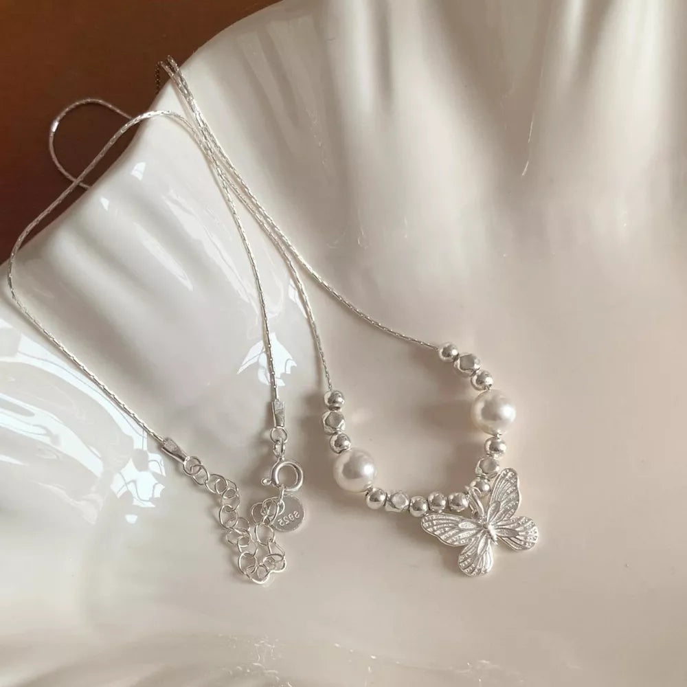 Silver necklace with pearl beads and a delicate butterfly charm.