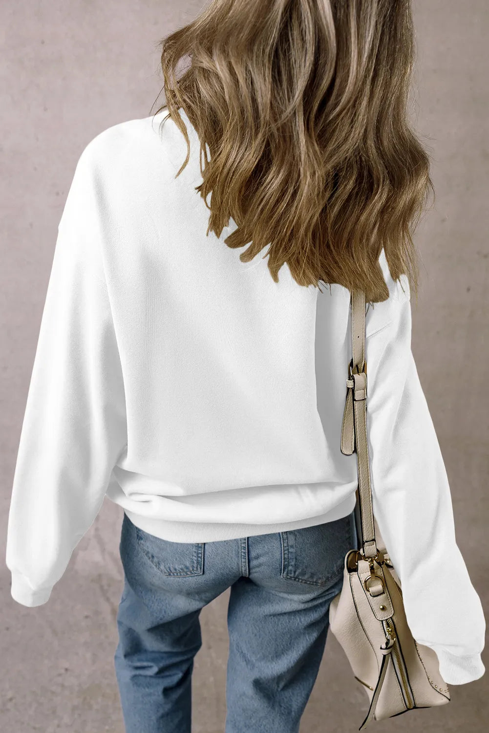 White crewneck sweatshirt with long sleeves, styled with jeans and a crossbody bag.