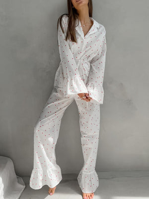 White cotton pajama set with red heart print, button-down top and ruffled pants.