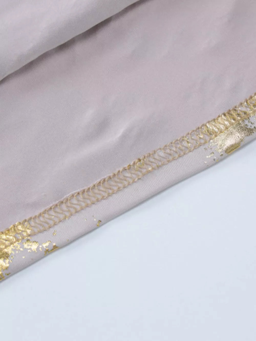 Cream maxi gown detail with abstract gold pattern and stitched hem.