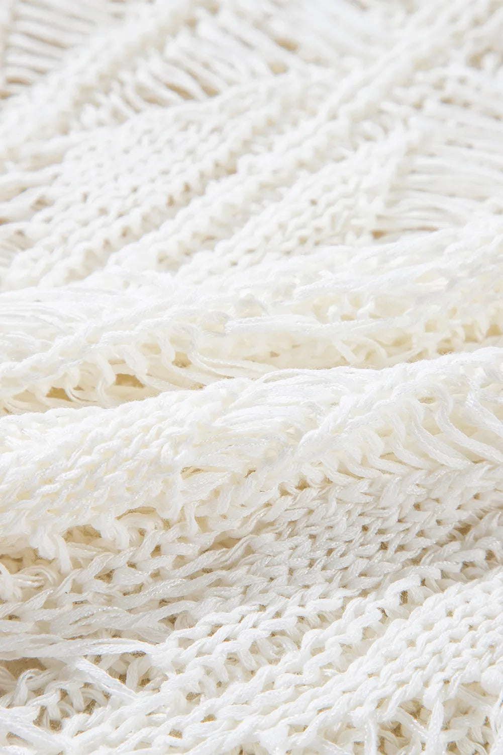 Open-knit crochet sweater in ivory with fringe detail and a cotton blend texture.