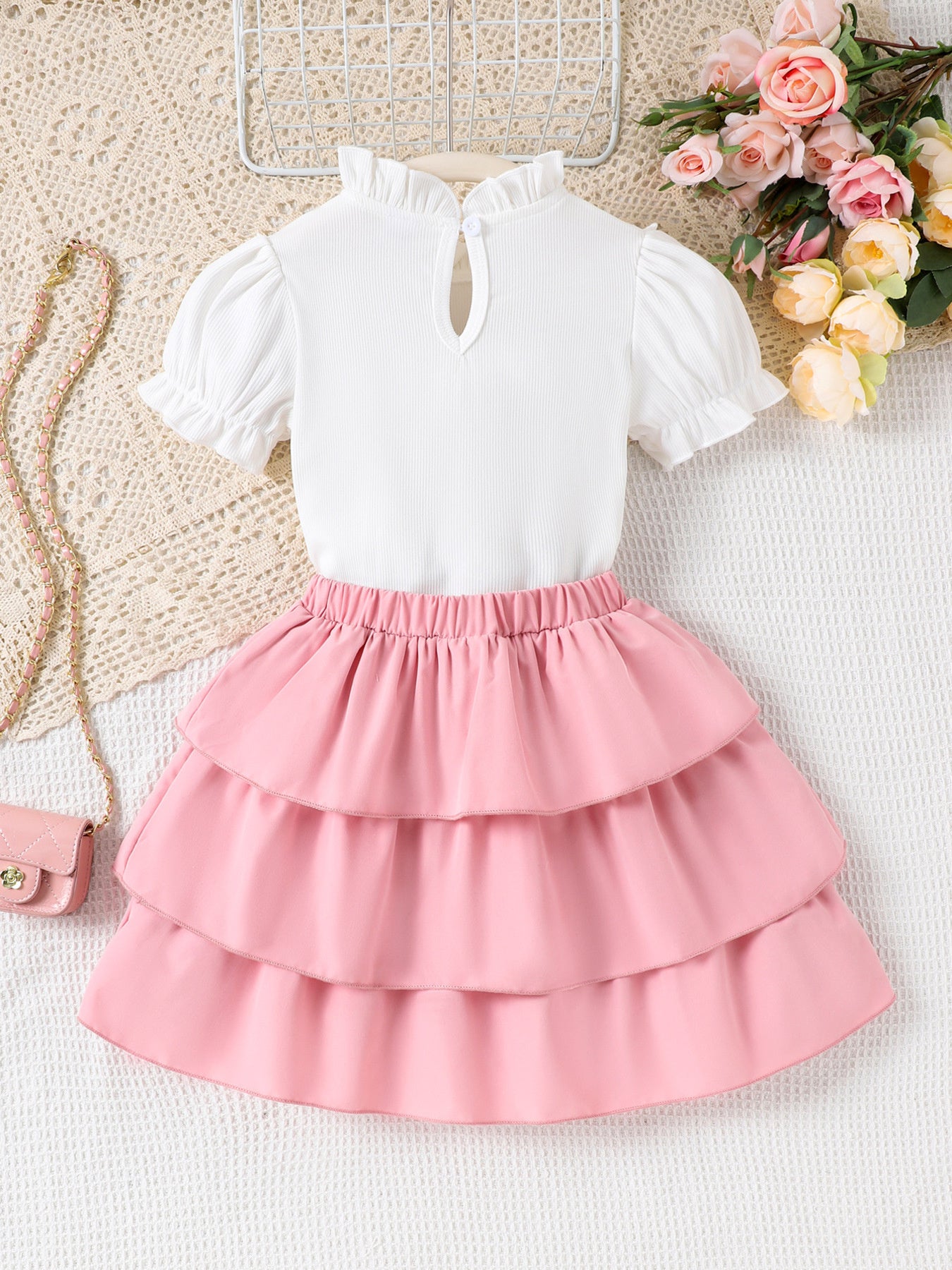 Toddler white ruffled mock neck top with puff sleeves and pink tiered skirt with elastic waistband.