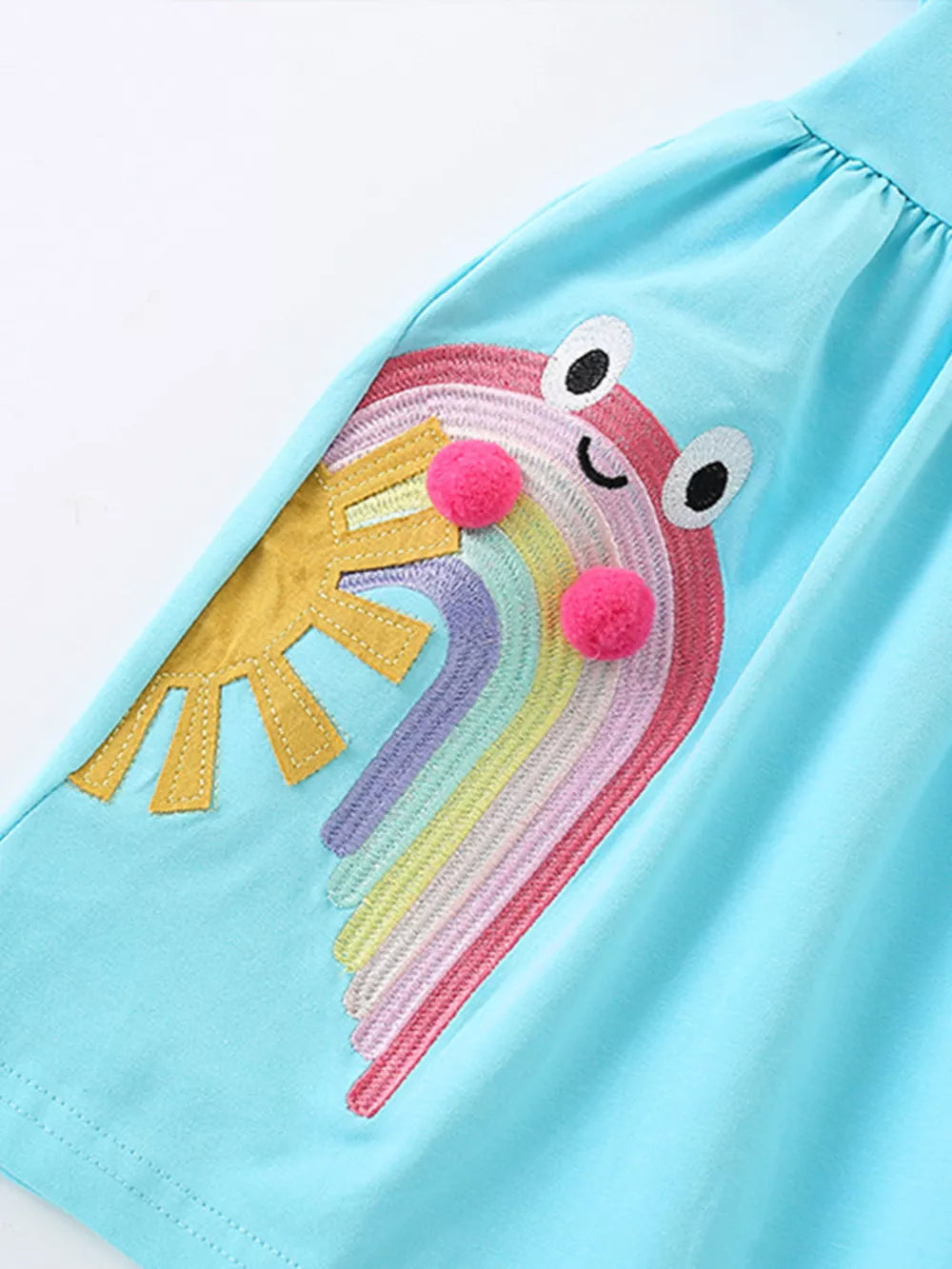Light blue cotton babydoll dress with rainbow embroidery, sun applique, and pom-poms.
