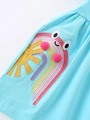 Light blue cotton babydoll dress with rainbow embroidery, sun applique, and pom-poms.