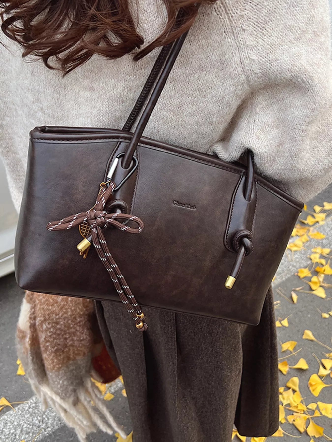 Brown leather shoulder bag with decorative knot and charm detail