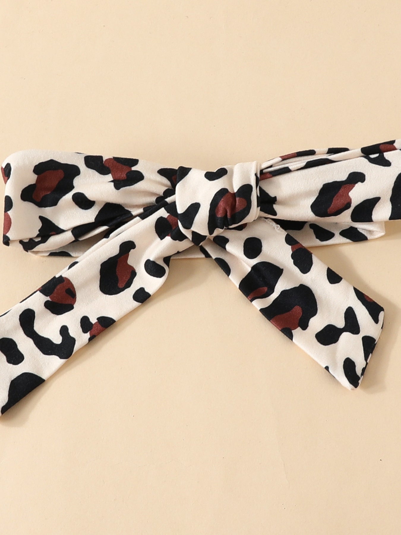 Baby bodysuit detail with leopard print and bow, 100% polyester.