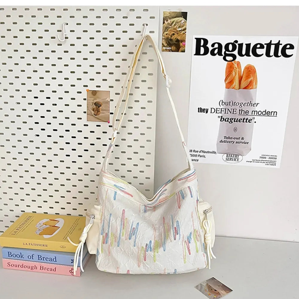 White slouchy shoulder bag with colorful embroidered abstract lines and side pockets.