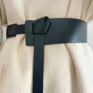 Black leather belt with knot detail and elongated tail cinching a cream sweater.