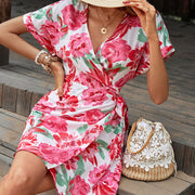 Floral wrap mini dress with flutter sleeves and a tie waist, styled with jewelry and a straw bag.