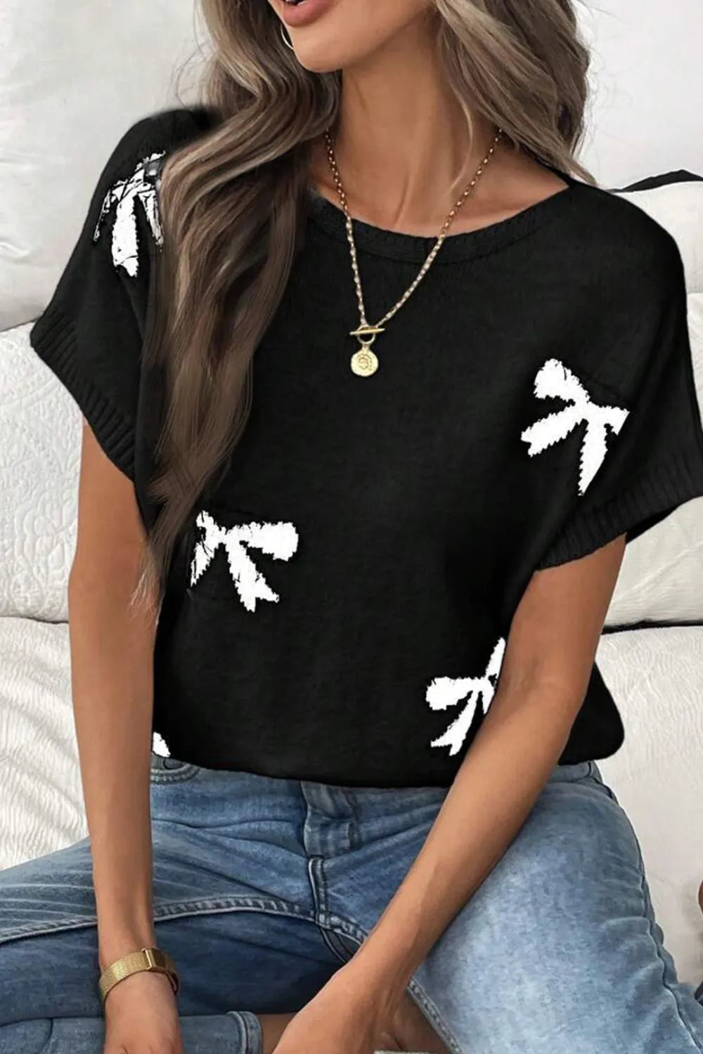 Black knit tunic with white bow motif, short sleeves, and crew neck.