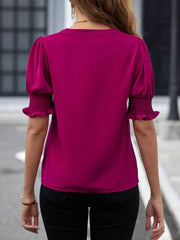 Cerise blouse with puffed sleeves and ruched cuffs, V-neck detail visible.