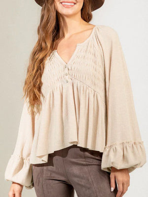 Tan textured ribbed peplum blouse with smocked bodice, button detail, and ruffled cuffs.