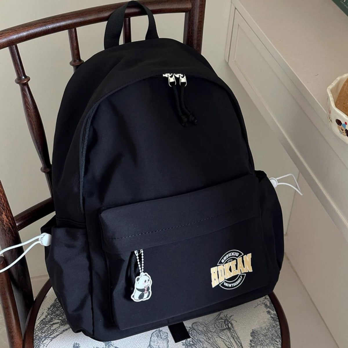 Black minimalist nylon backpack with front pocket, panda charm, and side drawstrings.