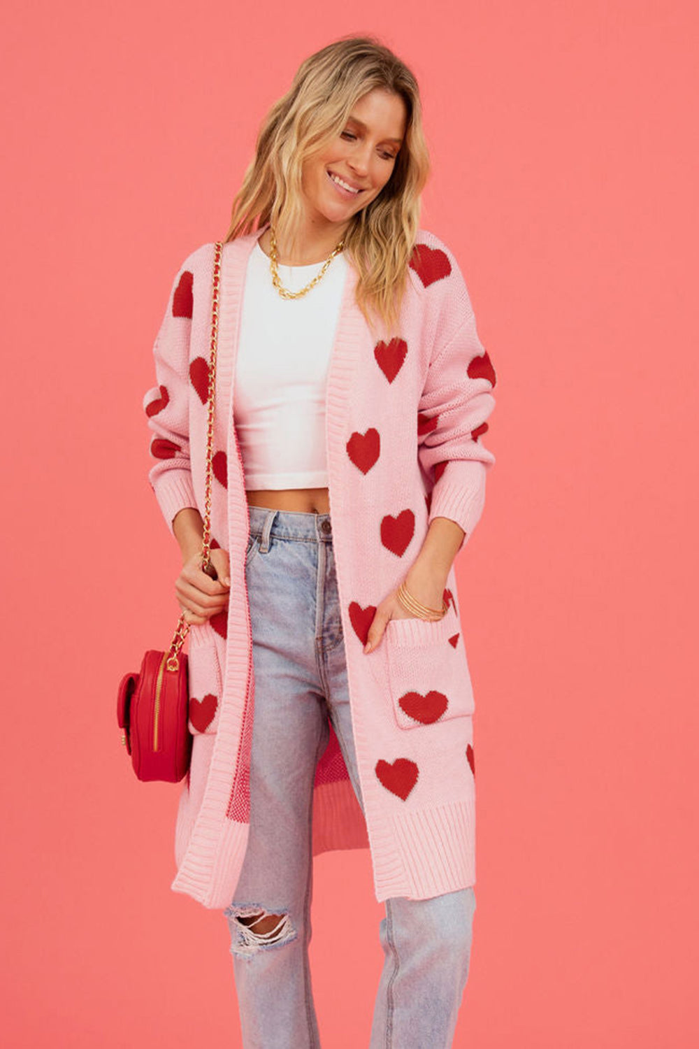 Blush pink longline knit cardigan with red heart motif, pockets, and open front.