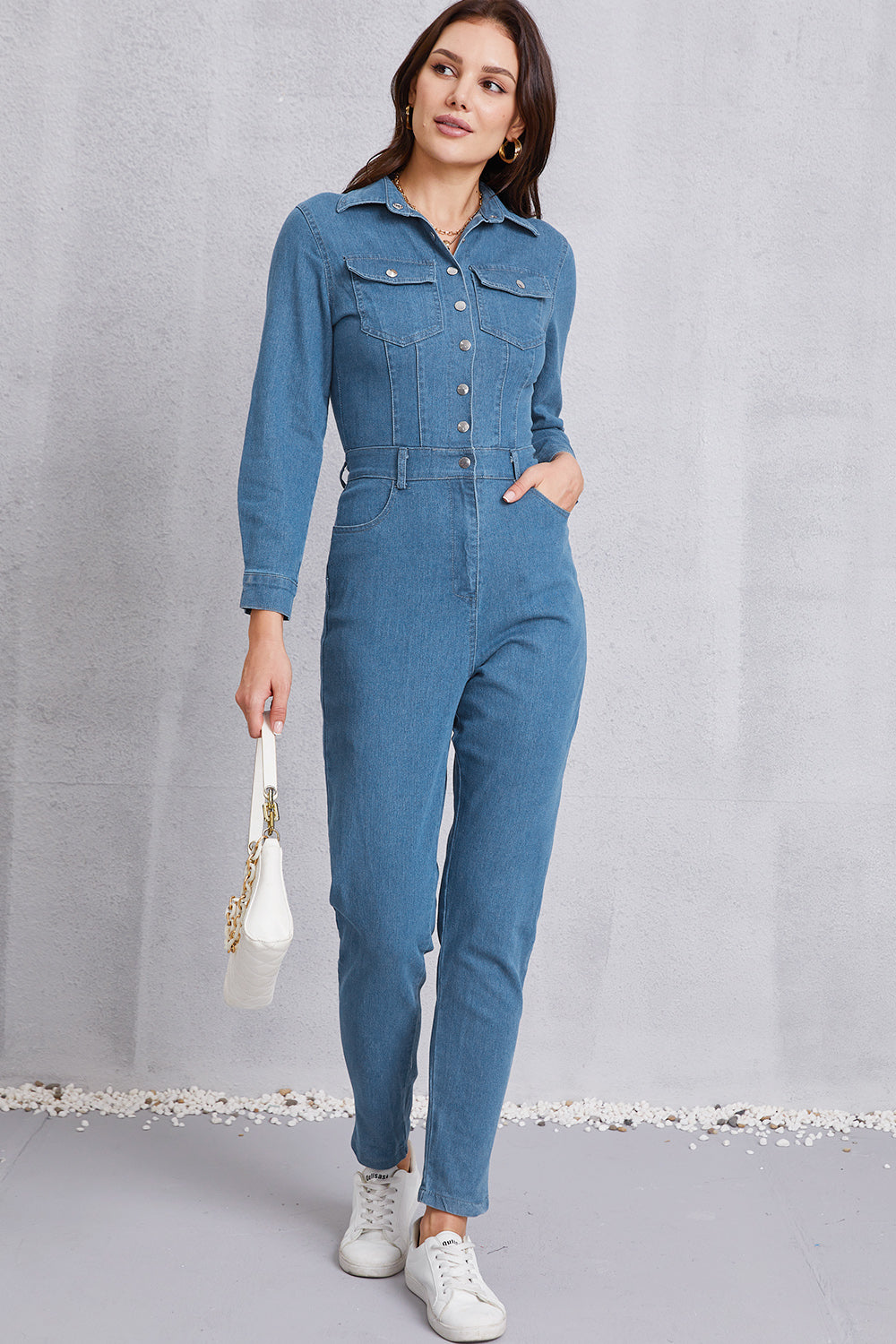 Denim utility jumpsuit in medium wash with defined waist, long sleeves, and button front.