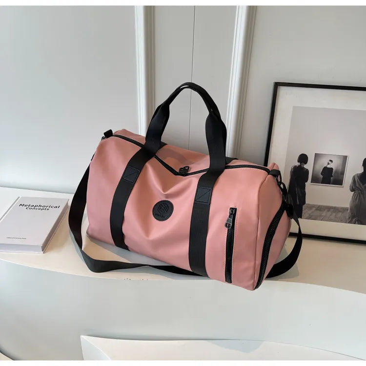 Dusty pink canvas duffel bag with black contrast straps and zipper details.