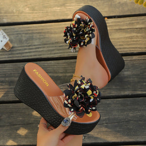 Black wedge sandals with multicolor floral pom-poms and clear straps.
