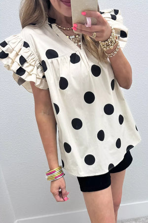 Cream cotton v-neck shirt with black polka dots and ruffled short sleeves.