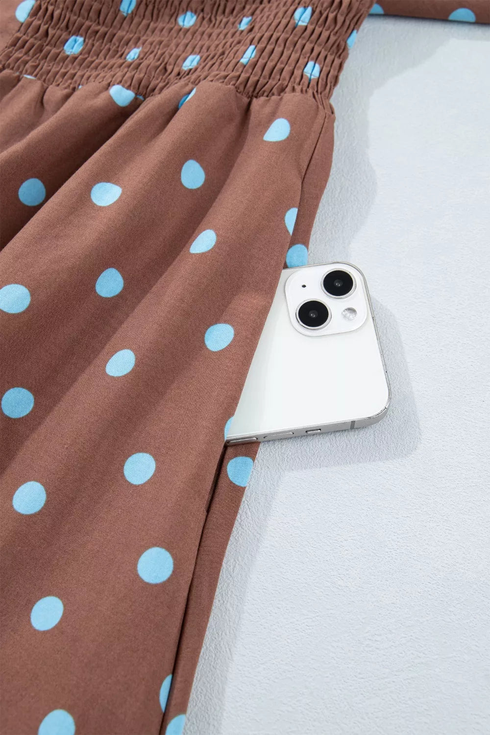 Brown polka dot midi dress with smocked bodice and side pocket holding a phone.