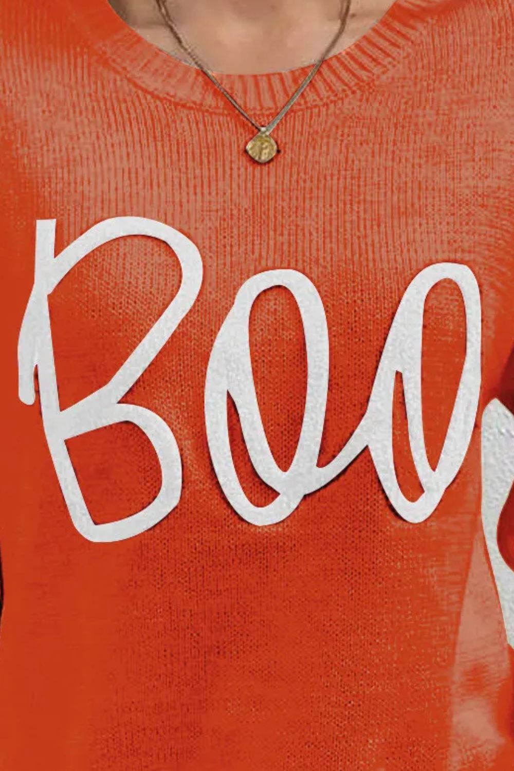 Orange crewneck sweater with white "Boo" appliqué and a delicate necklace.
