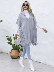Textured knit poncho in dark gray with fringe, wooden buttons, and a hooded neckline.