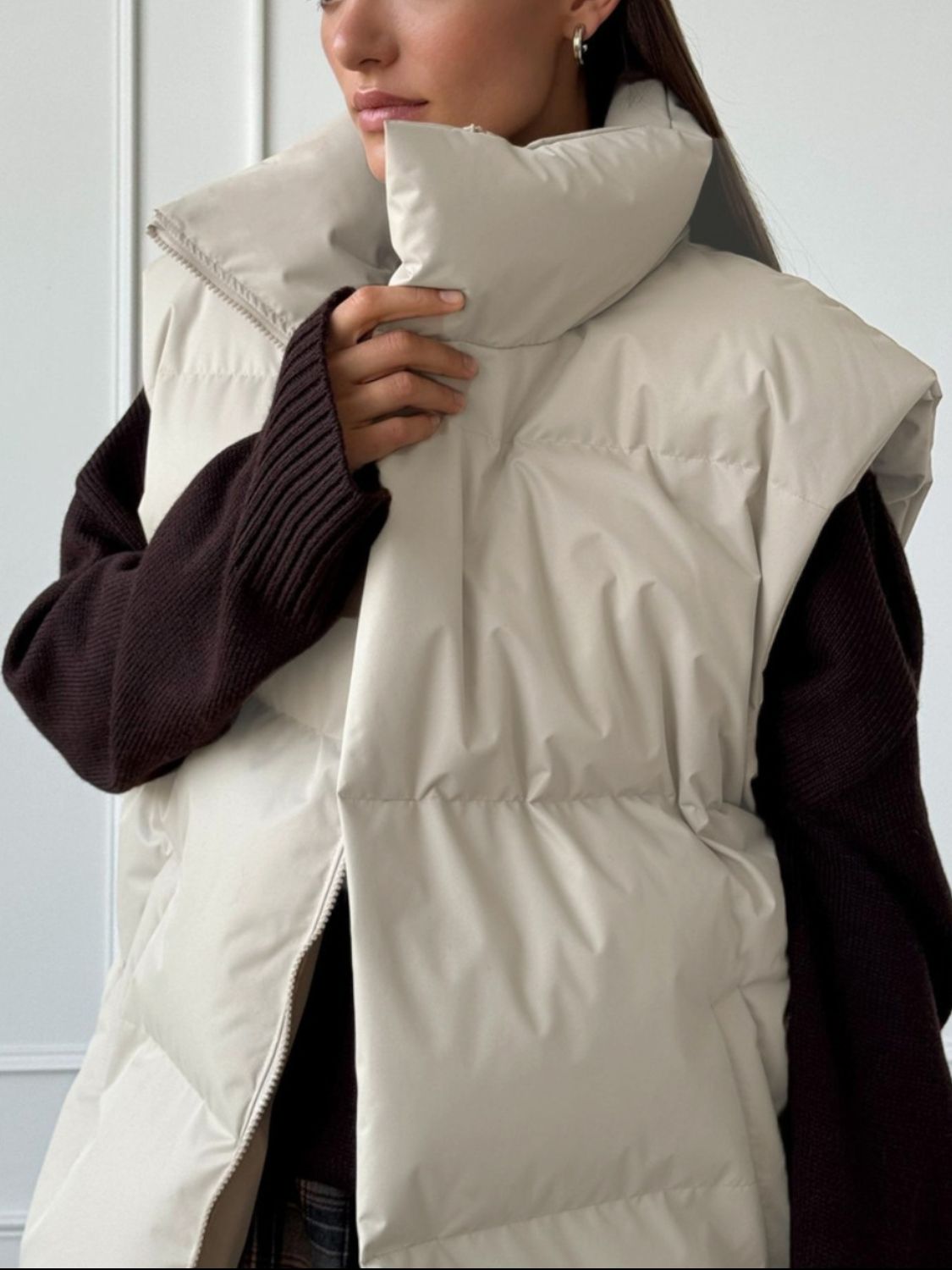 Padded puffer vest in Dust Storm with a high collar and zip front, layered over a dark sweater.