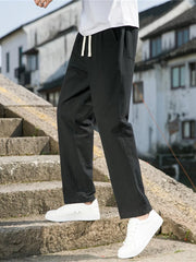 Black drawstring sweatpants with pockets on a man walking on stone stairs.