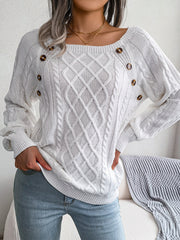 White cable-knit sweater with buttoned shoulder detail and diamond pattern.