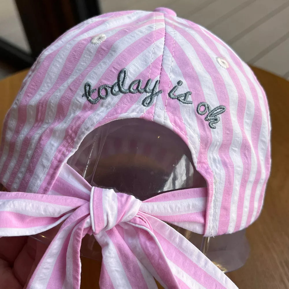 Pink and white striped cotton baseball cap with embroidered text and a bow tie back.