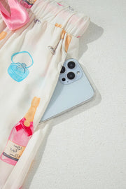 White silk pajama pants with champagne print and pink bow detail, showing a phone in the pocket.