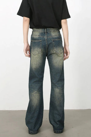 Distressed flare jeans in medium wash denim with a faded, worn look and subtle graffiti-style marks.