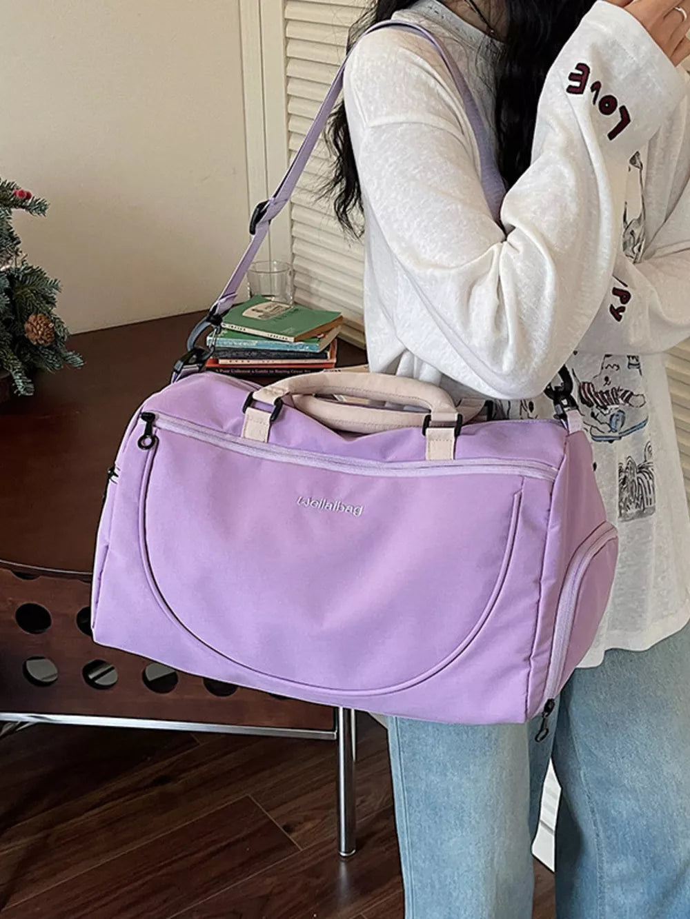 Purple duffle bag with adjustable strap and embroidered detail, worn by a woman.