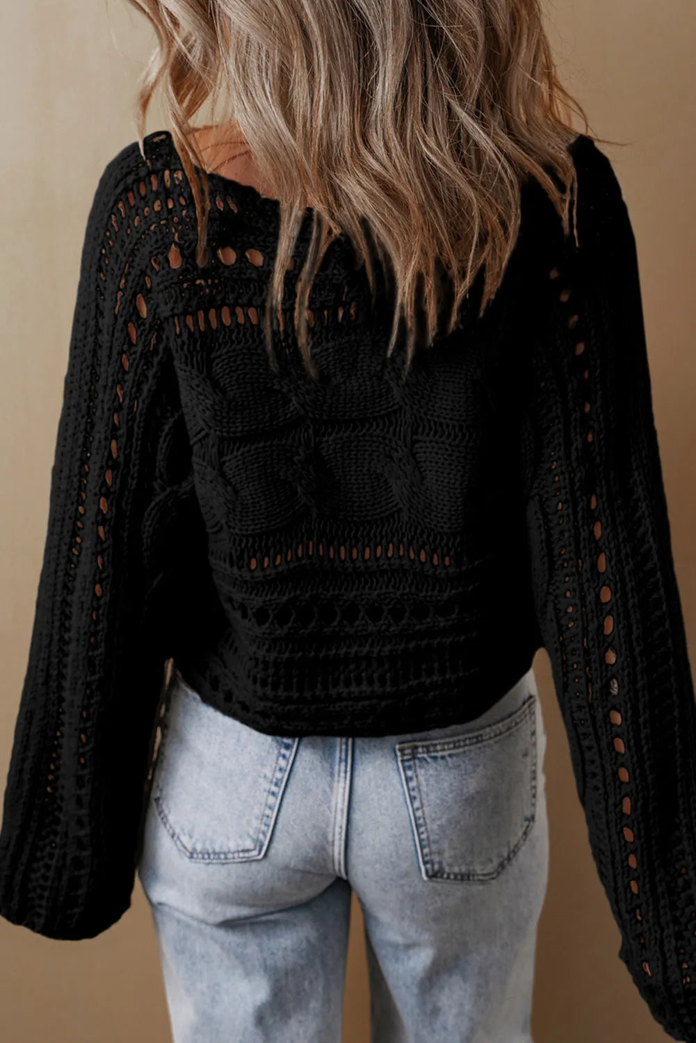 Black cable knit sweater with cutout details and long sleeves.