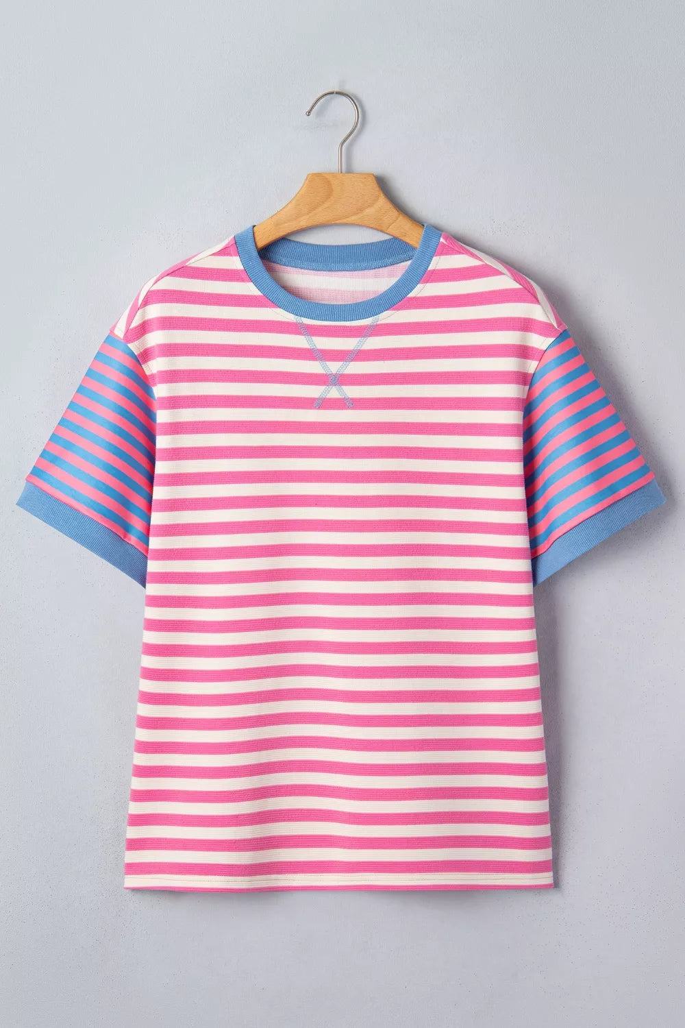 Short sleeve t-shirt with pink and white horizontal stripes, blue striped sleeves, and blue crew neck.