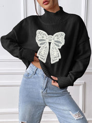 Black turtleneck knit sweater with white lace bow appliqué, ribbed cuffs and hem.
