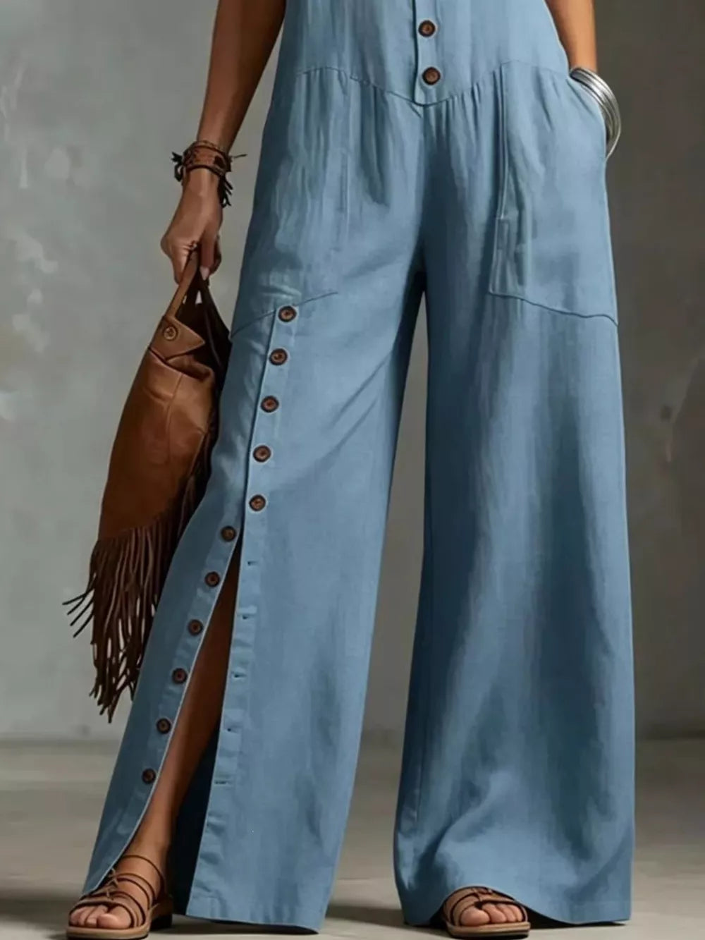 Blue wide-leg jumpsuit with button details and pockets, styled with a fringe bag.