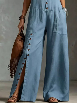 Blue wide-leg jumpsuit with button details and pockets, styled with a fringe bag.