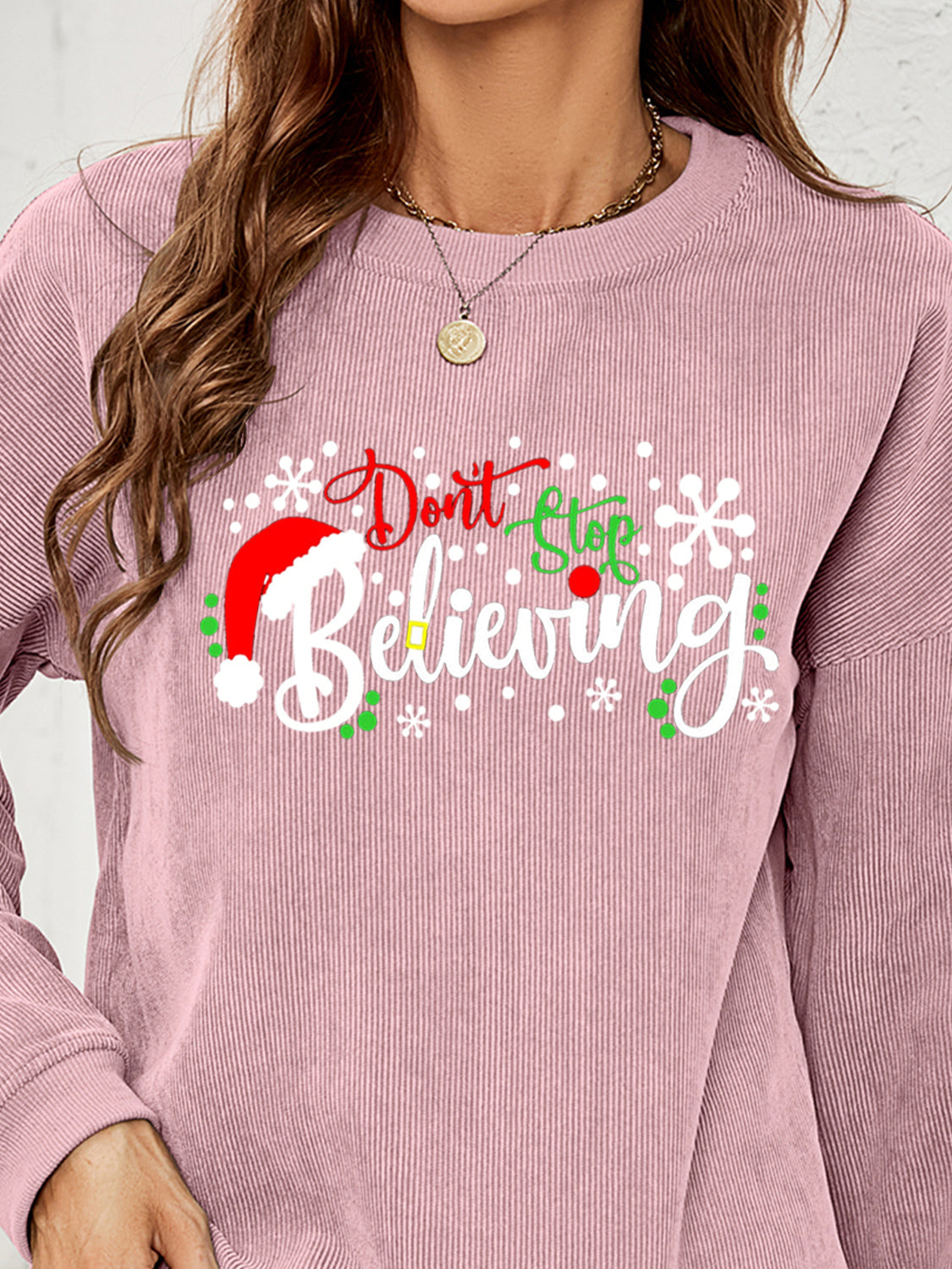Dusty Pink corduroy crewneck sweatshirt with "Don't Stop Believing" Christmas graphic and Santa hat detail.