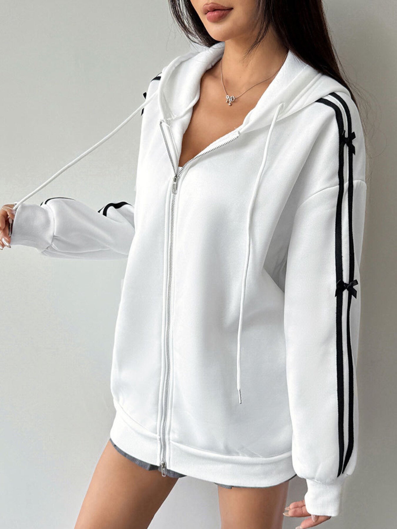 White zip-up hoodie with black stripes and bow details on sleeves.