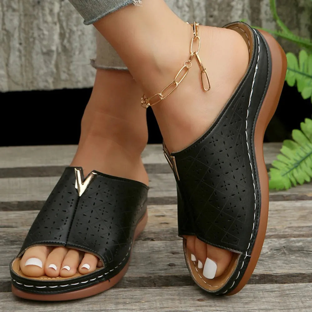 Black laser-cut leather platform slides with V-detail and white stitching.