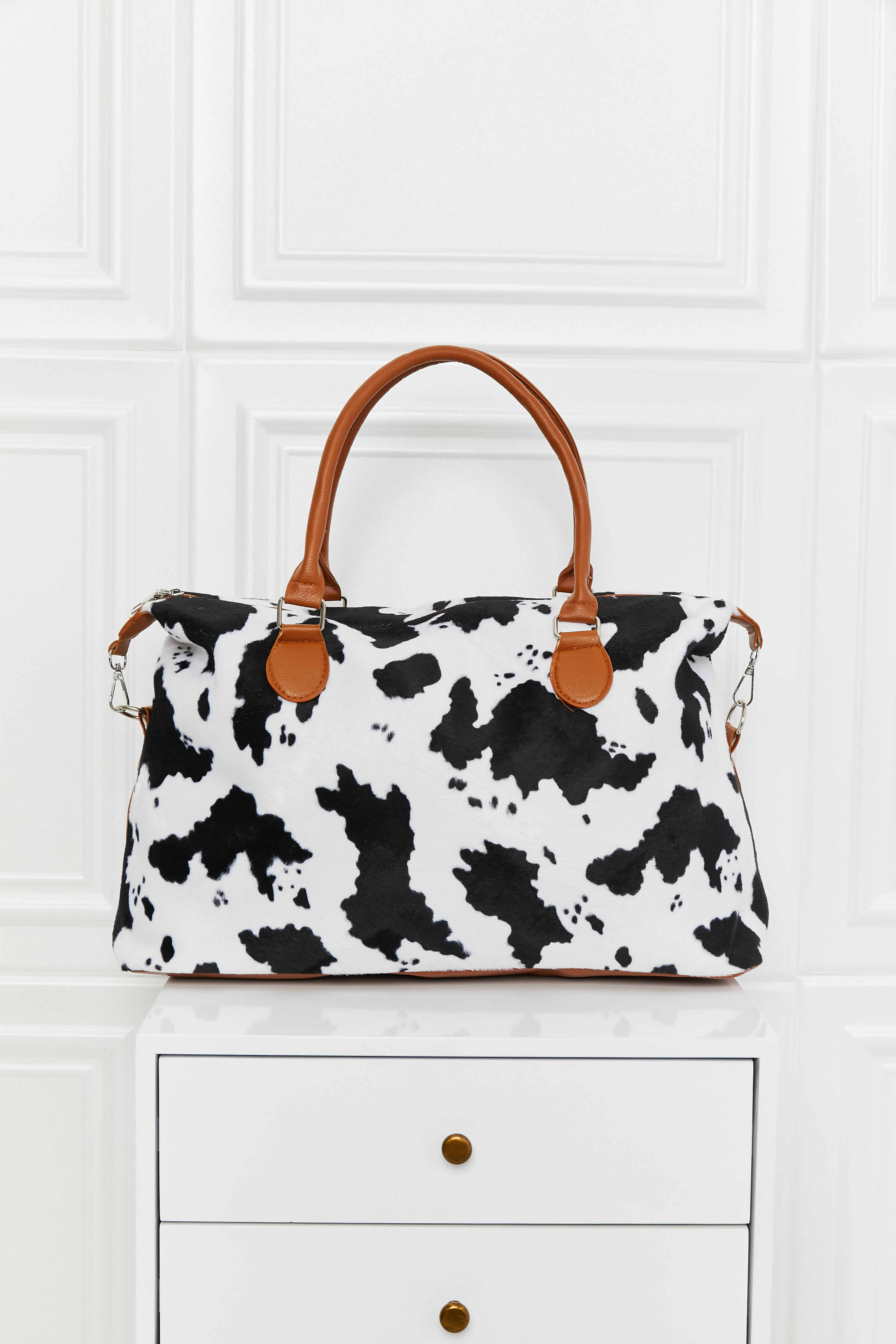 Satchel bag with cow print, brown leatherette handles and trim.
